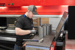 An employee measuring metal pieces with a tape measure.