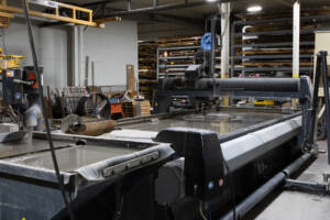 Large Black Water Jet Machine in action cutting custom metal pieces.