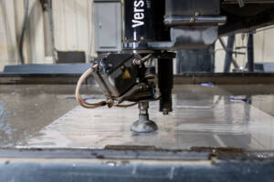 A closeup photo of a water jet machine head cutting metal pieces.
